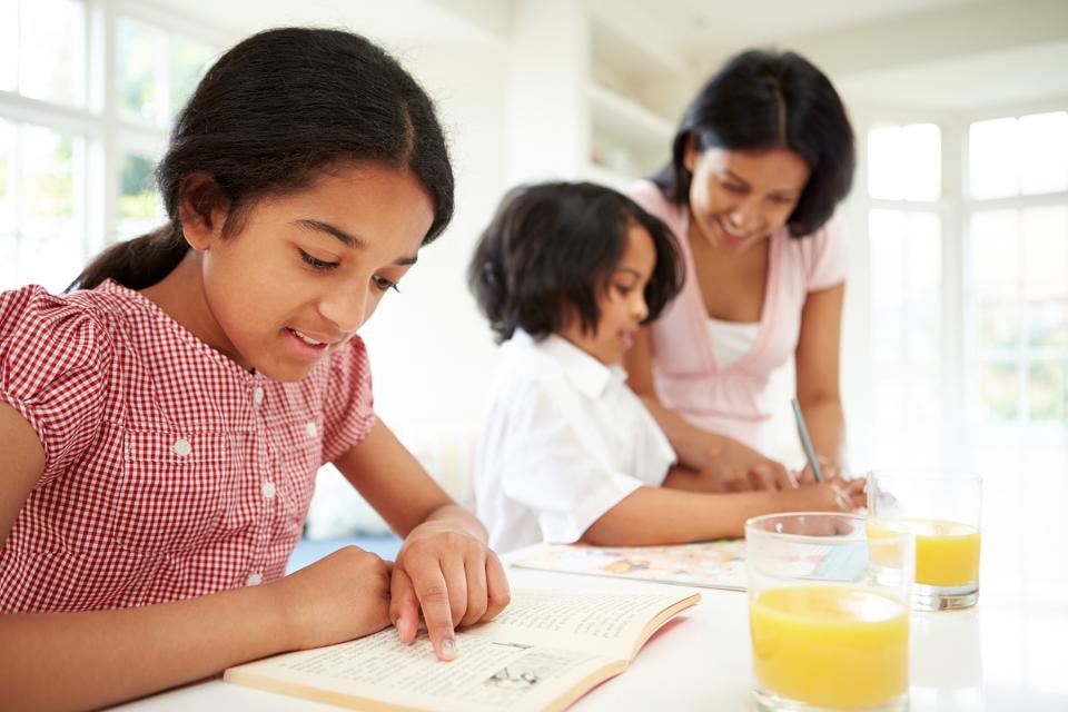 Siblings sit at the kitchen counter with their mother as she helps them with their reading.