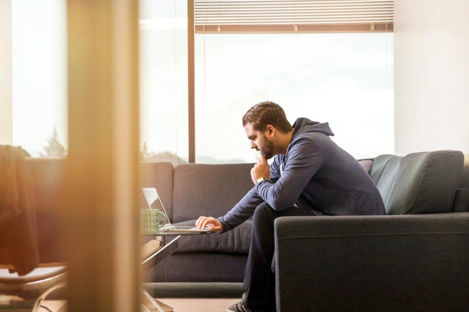 Man sits on the couch while using his computer.