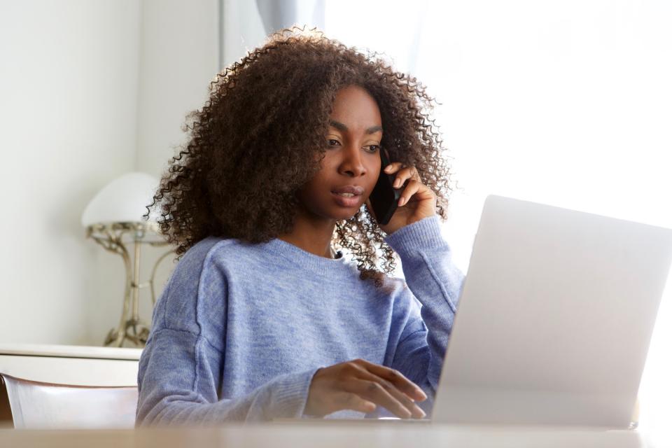 Woman uses a laptop computer and talks on a phone at the same time