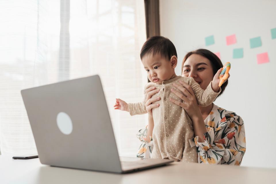 Mom holding baby up to video call on laptop.